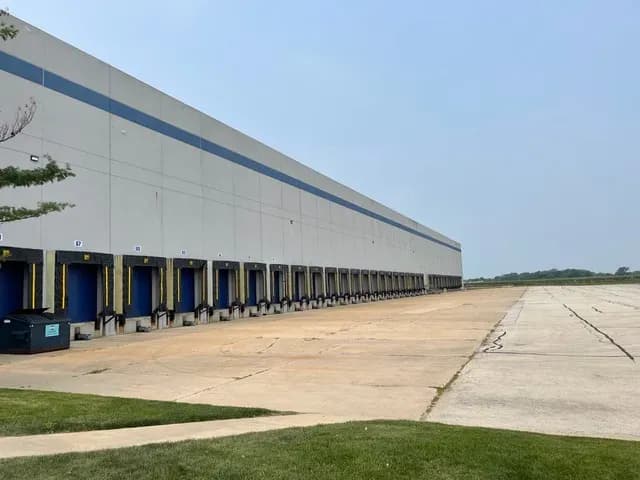 Large industrial warehouse with multiple loading dock doors and expansive concrete parking lot.